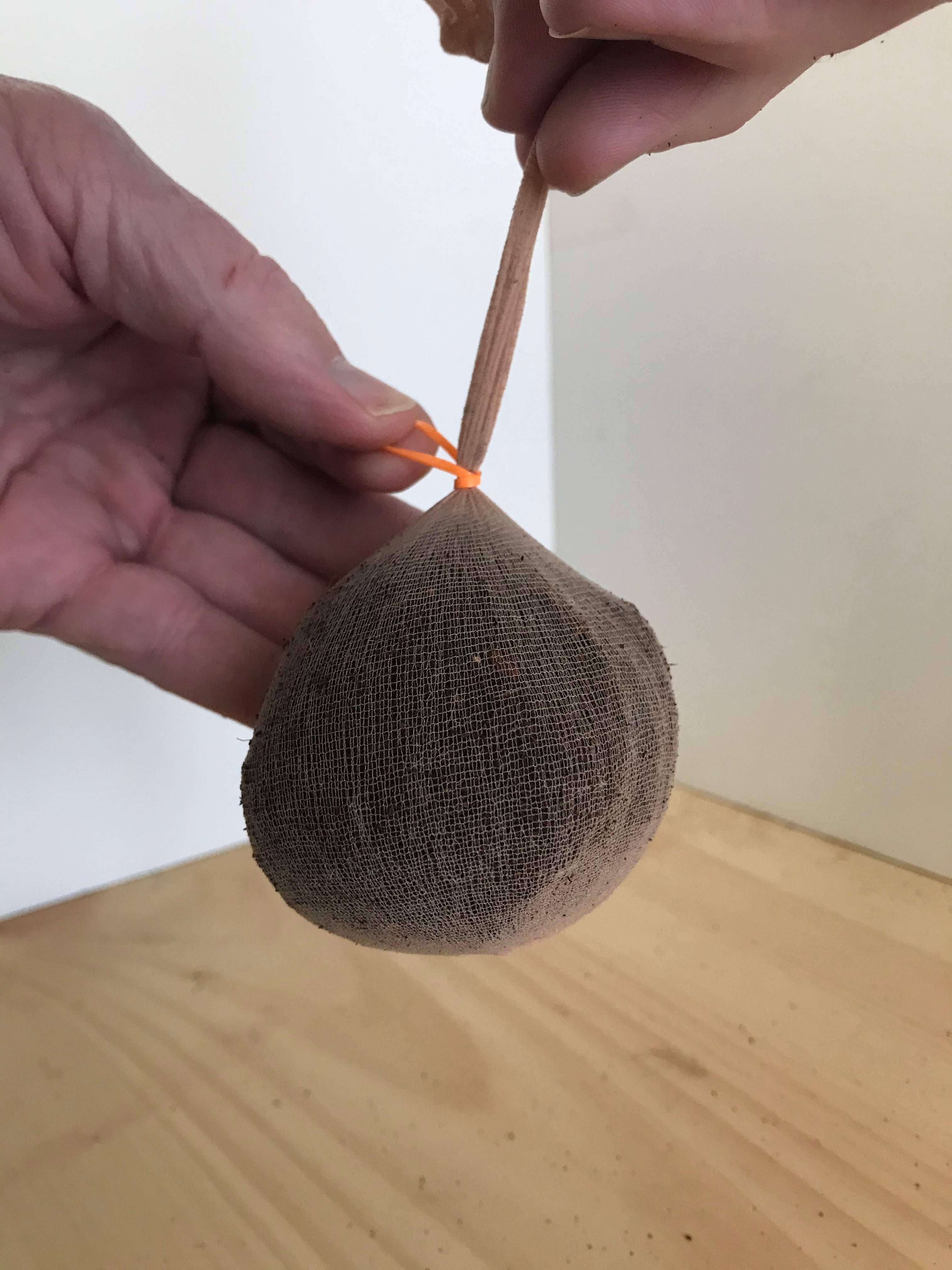 Brown fabric ball with a rubber band  being tied around it on a wooden surface.