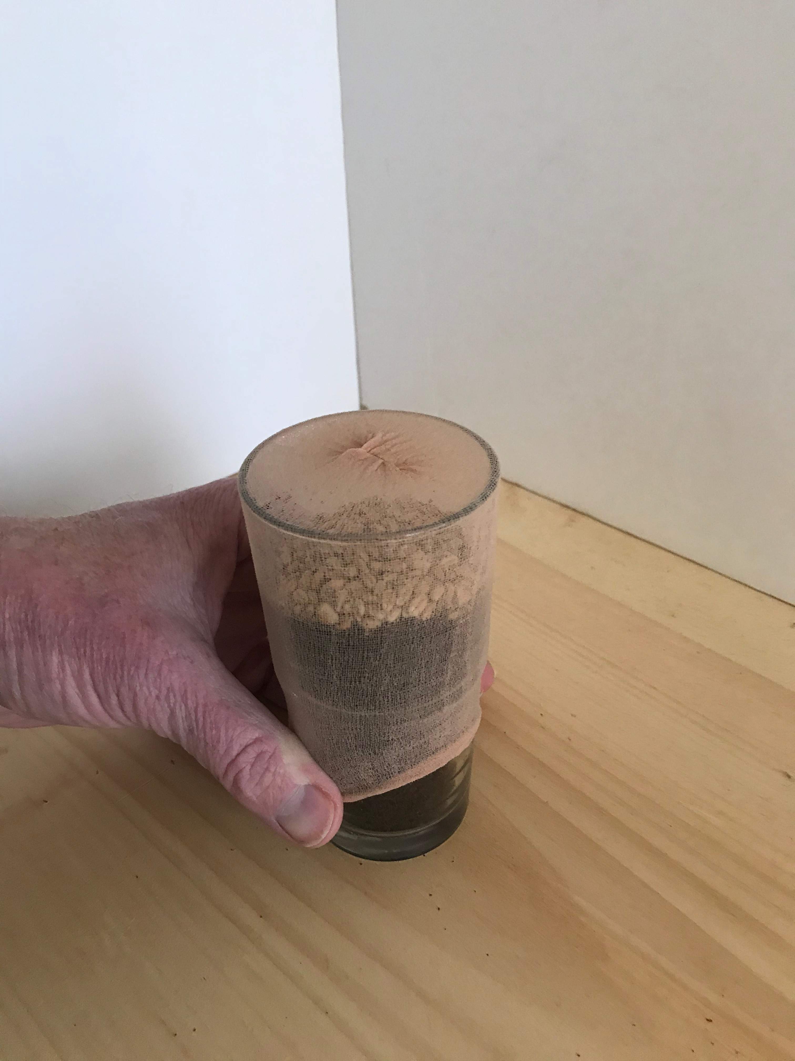 Hand sliding a sock over a glass on a wooden surface.